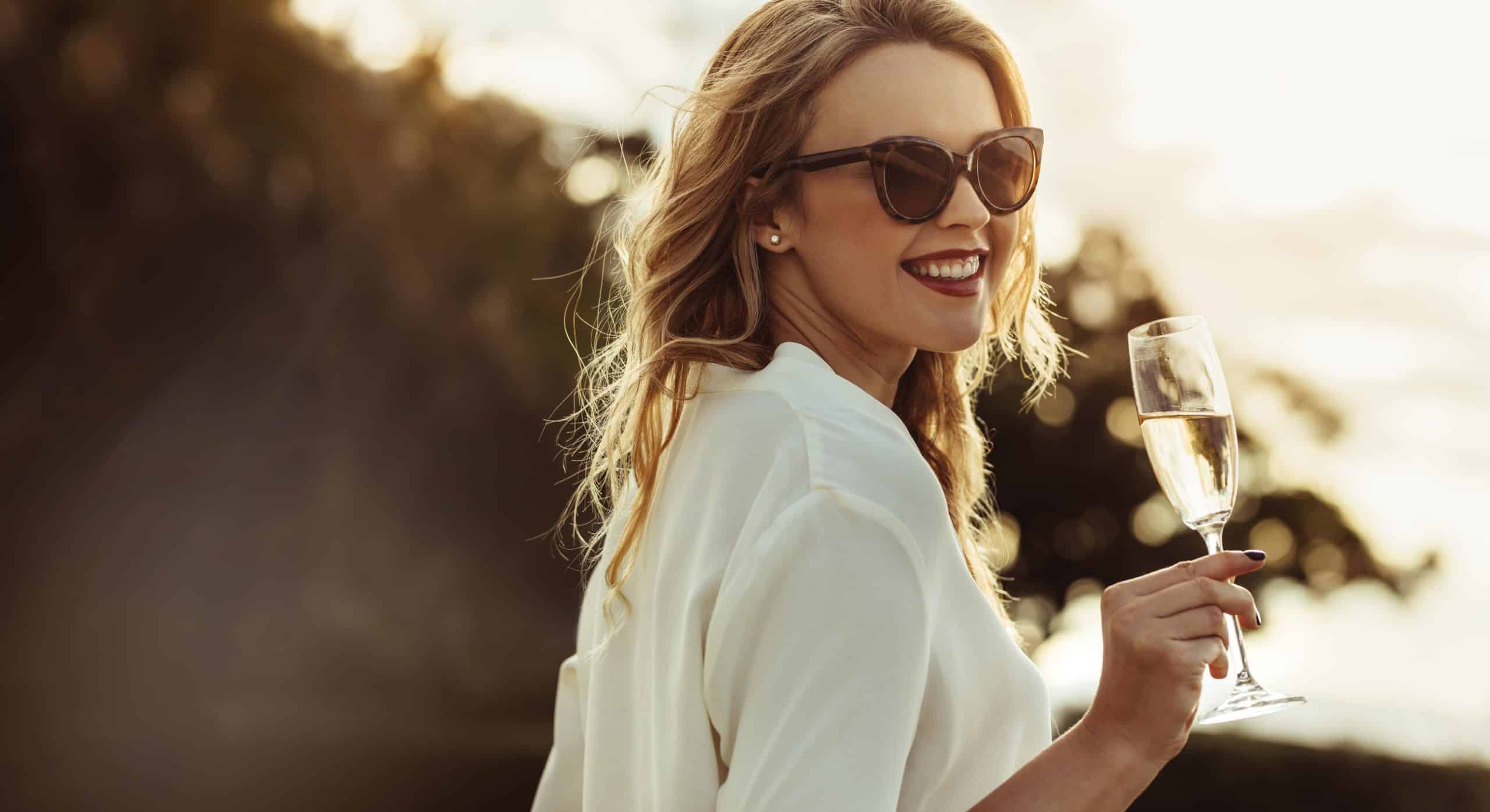 elegant-woman-in-sunglasses-with-a-glass-of-wine-outdoors-smiling-caucasian-female-having-wine-min